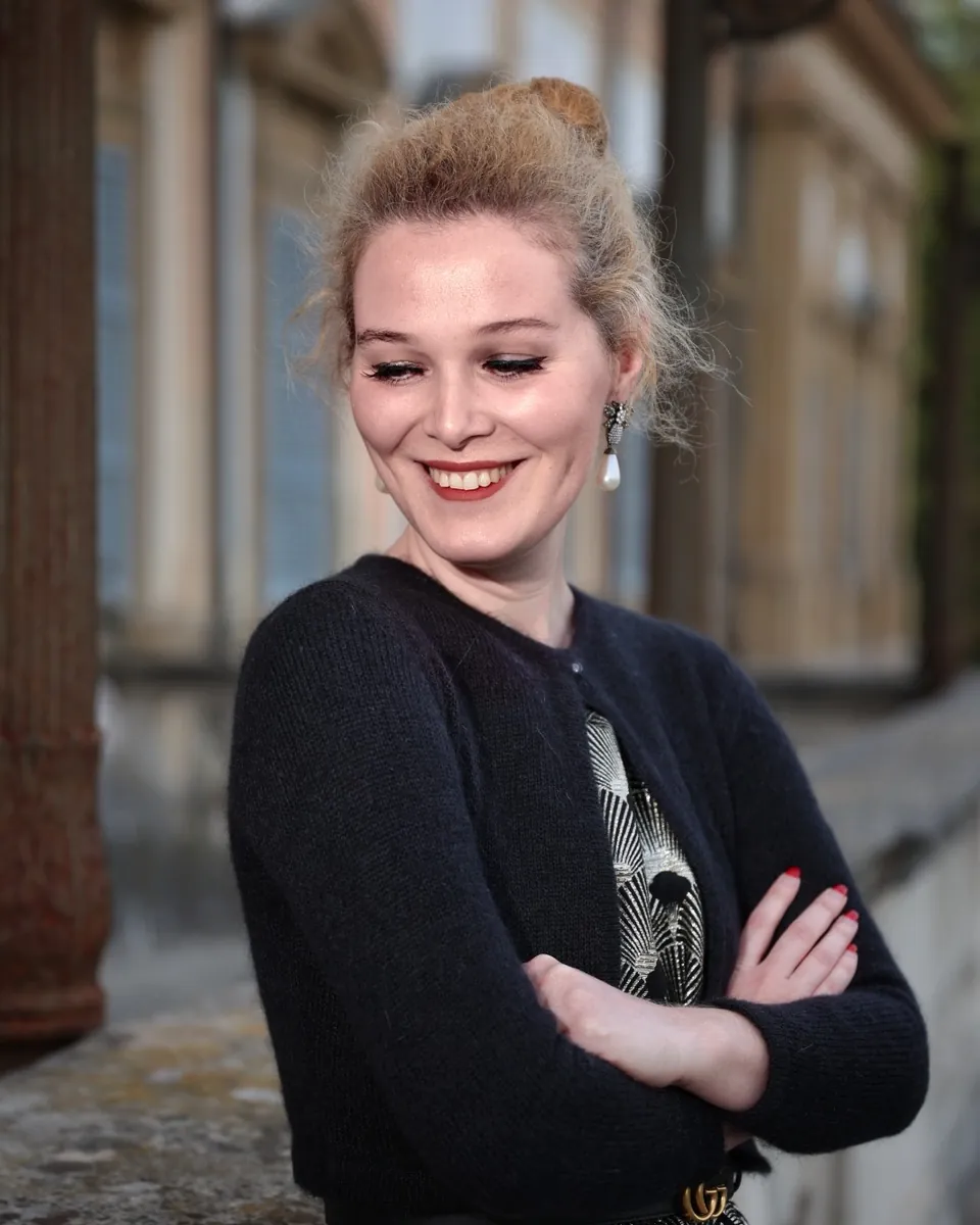 Il soprano Sofia Maria Riva sorride guardando verso il basso, a braccia conserte